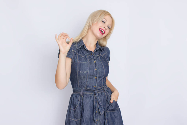 Studio portrait of a blonde woman in a denim dress. Girl posing against white background - Foto, afbeelding
