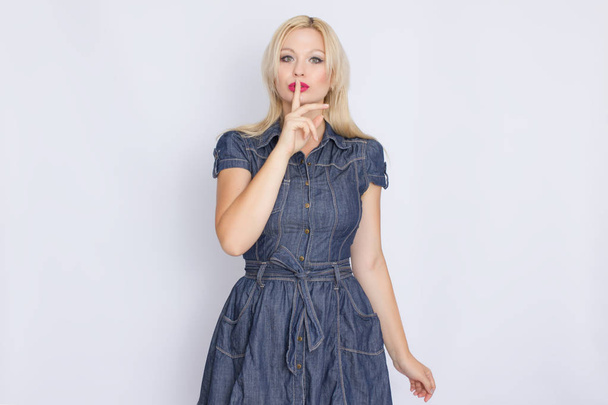 Studio portrait of a blonde woman in a denim dress. Girl posing against white background - Photo, image