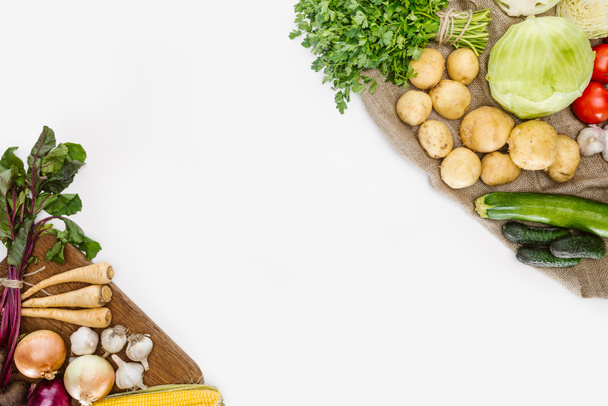 верхний вид организованных сырых овощей на деревянной разделочной доске и мешковины изолированы на белом
 - Фото, изображение
