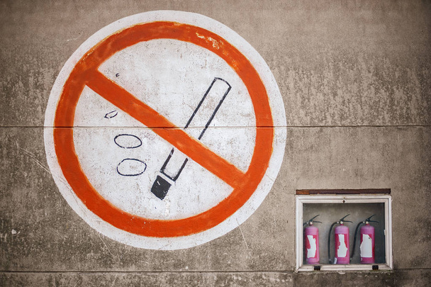 Big sign on concrete wall with no smoking sign and three fire extinguishers on a side - Foto, Imagem