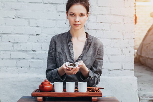Young woman sitting in meditation pose in front of tea set and aroma sticks. Relaxation concept - Fotografie, Obrázek