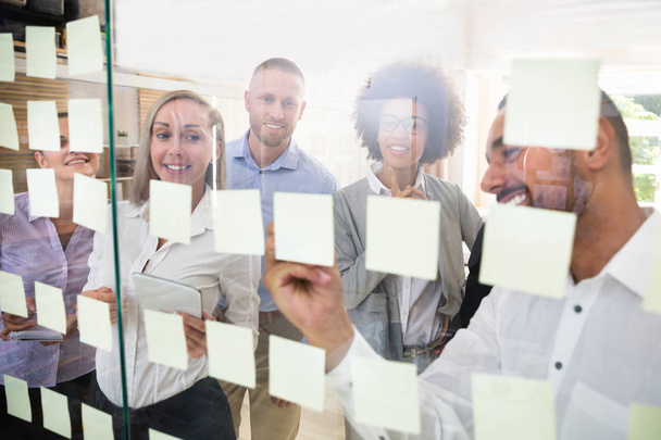 Group Of Young Businesspeople Sticking Adhesive Notes On Transparent Glass Wall In Office - Photo, Image