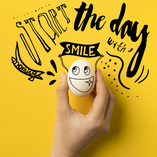 cropped image of woman holding egg isolated on yellow with "Start the day with a smile" inspiration - Photo, Image