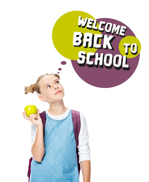 schoolchild holding apple and looking up at speech bubble with "welcome back to school" lettering, isolated on white - Photo, Image