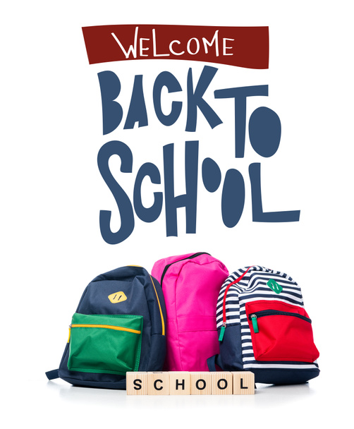 three colored schoolbags and wooden cubes with word school isolated on white, with "welcome back to school" lettering - Fotó, kép