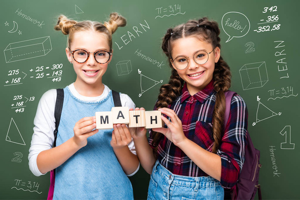 Schüler halten Holzwürfel mit Wort Mathe neben Tafel mit Mathematik-Symbolen - Foto, Bild