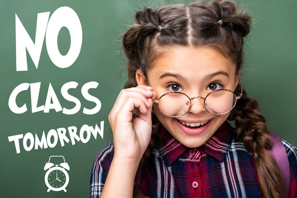 retrato del escolar mirando por encima de las gafas cerca de la pizarra, con letras de "no hay clase mañana"
 - Foto, Imagen