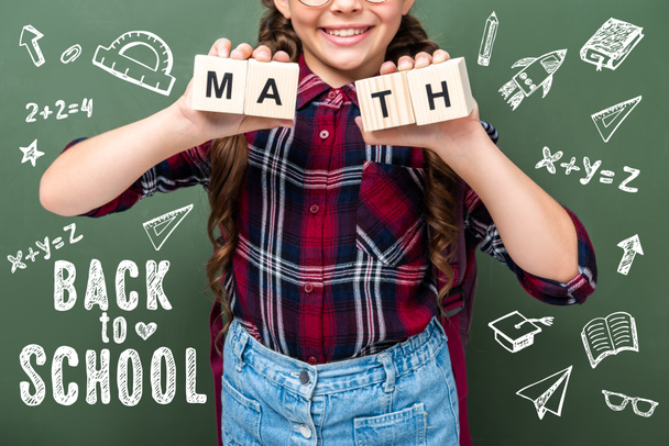 imagen recortada de escolar sosteniendo cubos de madera con palabras matemáticas cerca de pizarra con letras de vuelta a la escuela
 - Foto, imagen