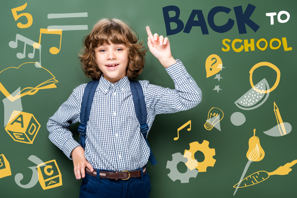 schoolboy showing idea gesture near blackboard, with icons and "back to school" lettering - Fotografie, Obrázek