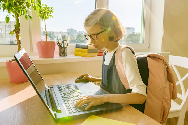 Petite étudiante de 8 ans en uniforme scolaire avec un sac à dos utilise un ordinateur portable. École, éducation, connaissances et enfants
 - Photo, image