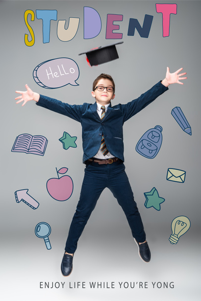 школьник в выпускной шапке прыжки, изолированные на серый с образовательными иконами и "студент - наслаждайтесь жизнью, пока вы yong" надписи
 - Фото, изображение