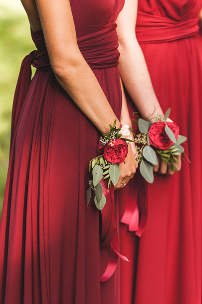  Παράνυμφοι στα κόκκινα φορέματα με βραχιόλια με βραχιόλια λουλούδι με κόκκινα τριαντάφυλλα και μεταξωτές κορδέλες, αμερικανικό ύφος γάμου  - Φωτογραφία, εικόνα