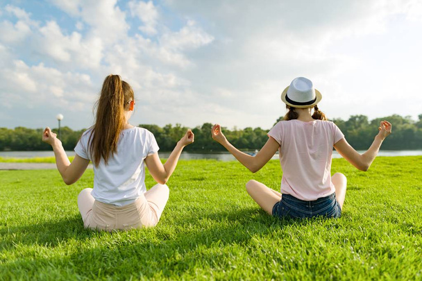 Two young girls doing yoga pose outdoor, yoga at sunset in the park, back view - Fotoğraf, Görsel