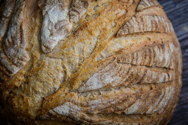 macro of whole handmade round white wheat bread lie on  dark wooden table - Фото, зображення