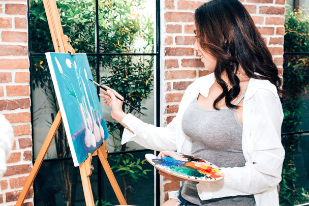 Молодая художница рисует на холсте с цветовой палитрой и акварельными красками дома
 - Фото, изображение