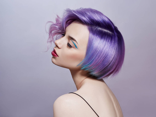 Portrait of a woman with bright colored flying hair, all shades of purple. Hair coloring, beautiful lips and makeup. Hair fluttering in the wind. Sexy girl with short  hair. Professional coloring - Фото, изображение