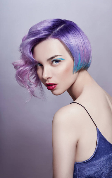 Portrait of a woman with bright colored flying hair, all shades of purple. Hair coloring, beautiful lips and makeup. Hair fluttering in the wind. Sexy girl with short  hair. Professional coloring - Photo, image