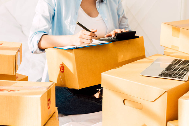 Jeune femme travaillant et check-list avec boîte en carton sur le lit à la maison - Business en ligne et concept de livraison
 - Photo, image