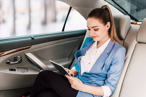 Businesswoman work with digital tablet computer and holding cup of coffee in back seat of luxury car - Foto, Bild