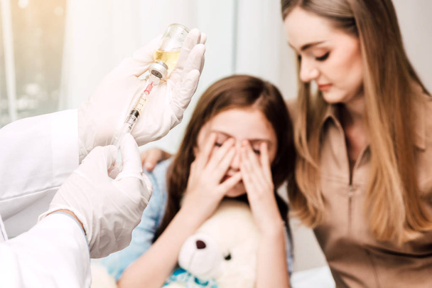 Doctor in de beschermende handschoenen geven injectie met kleine meisje kind en moeder op artsen tafel in hospital.healthcare en geneeskunde - Foto, afbeelding
