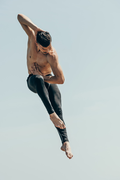 motion shot of handsome shirtless dancer in jump against blue sky - Photo, Image
