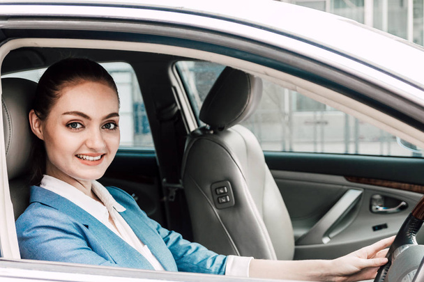 Mujer de negocios conduciendo su coche con una sonrisa y mirando a la cámara en el camino a la oficina
 - Foto, Imagen