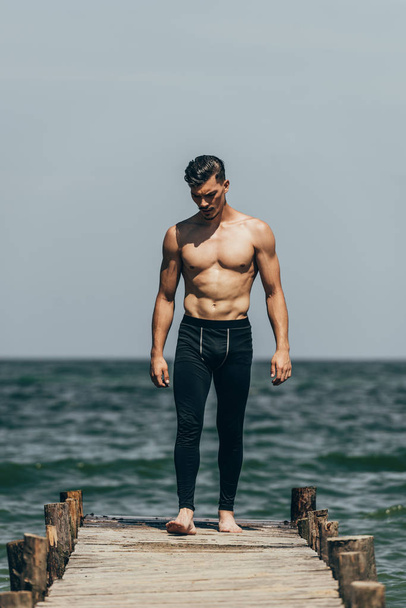 handsome sporty man standing on wooden pier - Foto, imagen