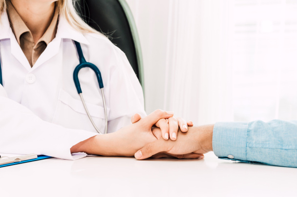 Ärztin berät und hält männliche Patientin beruhigend an der Hand auf dem Ärztetisch im Krankenhaus.Gesundheitswesen und Medizin - Foto, Bild