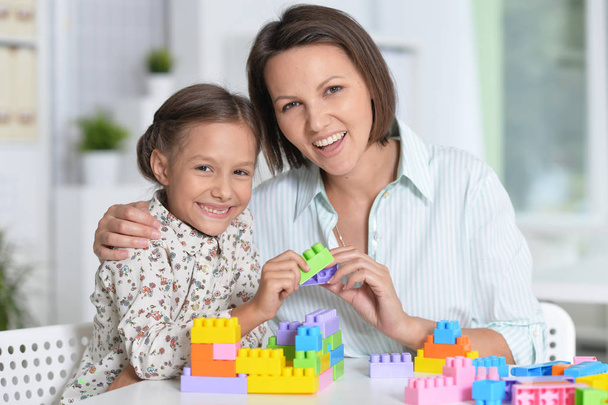 Kıvırcık küçük kız ve annesi renkli plastik blokları ile evde oynarken - Fotoğraf, Görsel