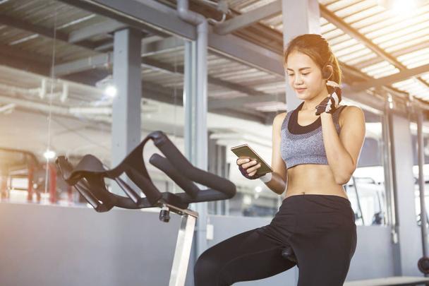 Sport woman cycling on machine in gym while listening to music. - Photo, Image