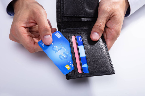 Die Hand einer Person entfernt die Kreditkarte aus der Brieftasche auf weißem Hintergrund - Foto, Bild
