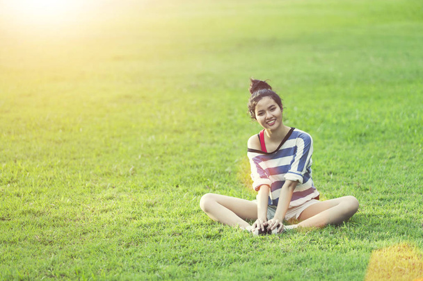 Mladá žena relaxovat a na zelené trávě s východem slunce ráno. Životní styl šťastný život. Dobrý zdravý koncept. - Fotografie, Obrázek