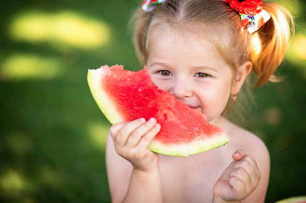 Πορτρέτο του ένα ξανθό κοριτσάκι με καρπούζι, καλοκαιρινή εξωτερική υγιεινό σνακ για τα παιδιά. Κοριτσάκι παίζει στον κήπο κρατώντας μια φέτα καρπούζι. - Φωτογραφία, εικόνα