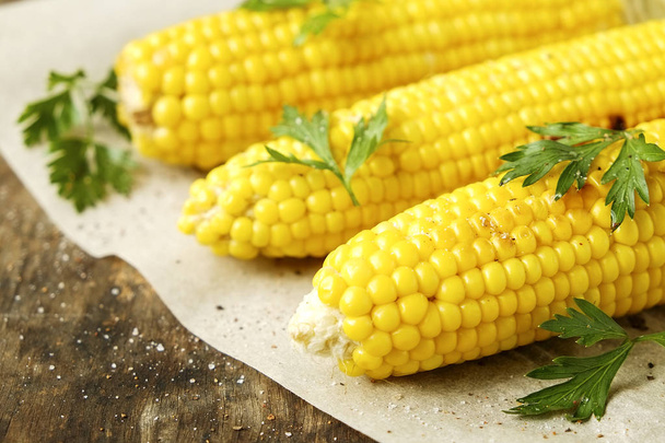 Three cobs of corn grilled on barbecue fire laid on dark stone table with parsley decoration. Healthy summer food concept. Clean eating habits. Background, top view, close up, flat lay, copy space. - Фото, изображение