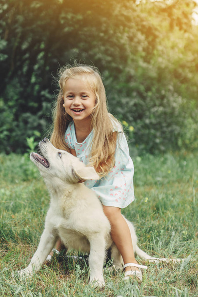 Little cute blond girl playing with her puppy golden retriever in summer in the park. - Foto, Imagem