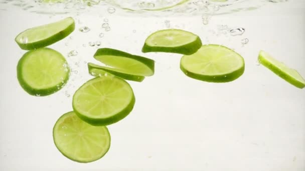 Round lime slices slowly sink in water, slow motion close-up - Footage, Video