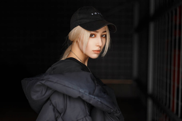 Retrato de Vogue de una joven hermosa con gorra negra y chaqueta de moda sobre un fondo oscuro
 - Foto, Imagen