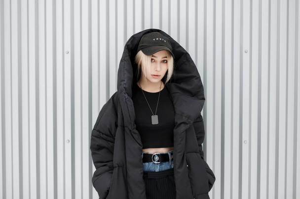 Мода красива жінка в чорній зимовій куртці з модною шапочкою на вулиці за волею металевої стіни
 - Фото, зображення