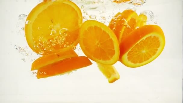 Oranje segmenten vallen in het water met spatten en bubbels, Slowmotion close-up - Video