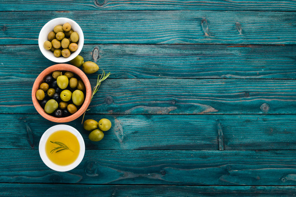 A set of olives and olive oil and rosemary. Green olives and black olives. On a blue wooden background. Free space for text. - Фото, изображение