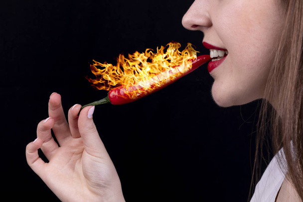 Menina come pimenta pimenta com fogo no fundo preto
 - Foto, Imagem