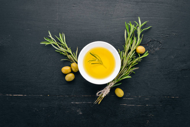 Olive oil in a plate and rosemary. On a black wooden background. Free space for text. - Фото, зображення