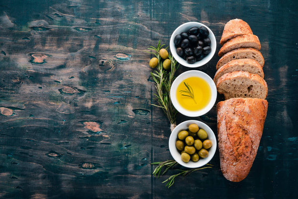 Olives and bread. Italian cuisine. On a wooden table. Top view. Free space for text. - Zdjęcie, obraz