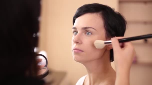 Der Visagist trägt einen großen Pinsel auf das Gesicht des Models auf - Filmmaterial, Video