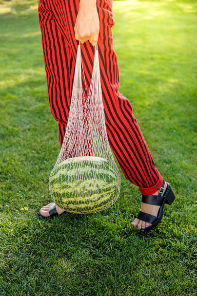 Close up fashion detail, young woman holding net bag with watermelon on a sunny summer day. Food fashion photo - Fotografie, Obrázek