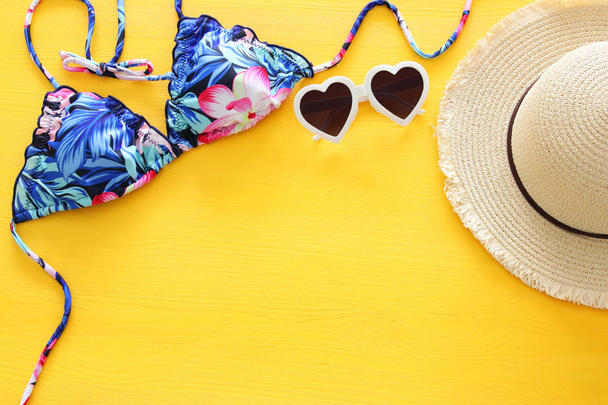 Top view of fashion female swimsuit bikini and white fedora hat over yellow wooden background. Summer beach vacation concept - Valokuva, kuva
