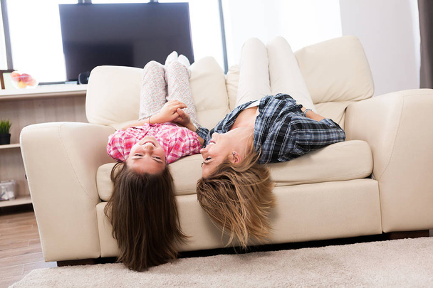 Beautiful mother with her cute daughter lying on the couch with their head upside down - Photo, Image