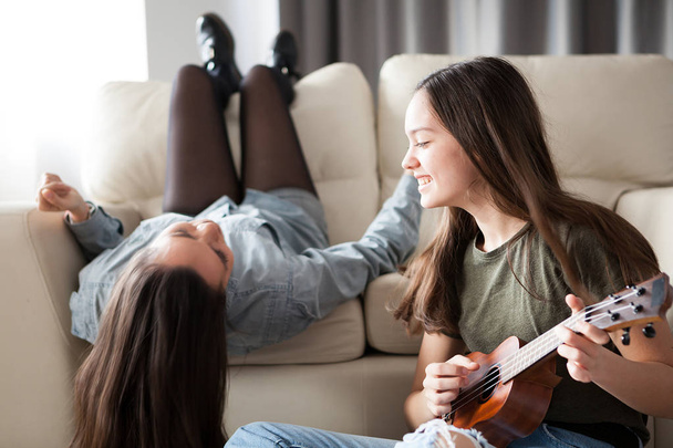 Een zus speelt aan de ukulele en de andere is zingen in de microfoon - Foto, afbeelding