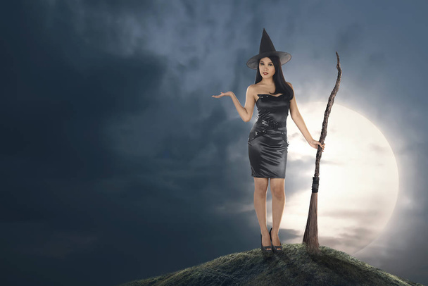 若いアジアの魔女帽子と月光背景にほうきの柄女性 - 写真・画像