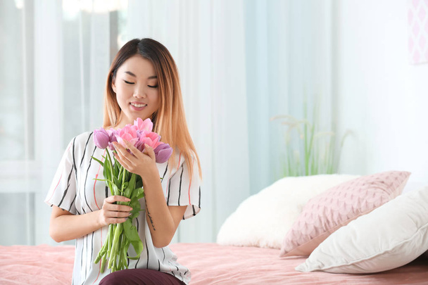 Beautiful smiling Asian woman with bouquet of tulips at home - Фото, зображення